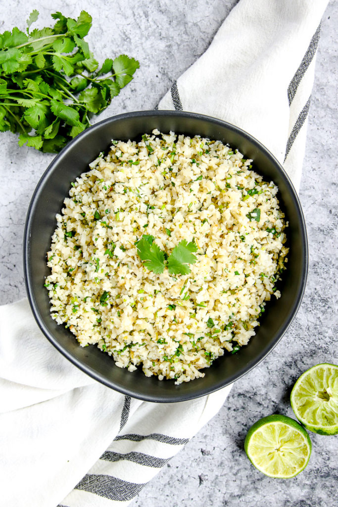 a black bowl on a striped napkin with cilantro lime cauliflower rice in it