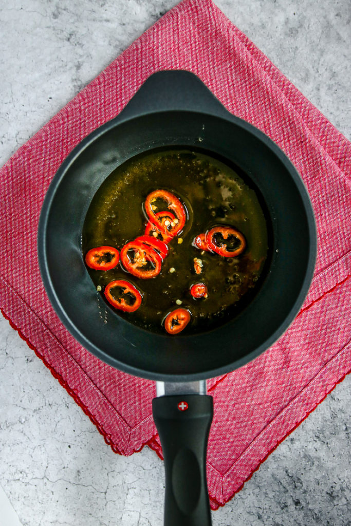 a saucepan of honey and sliced fresno chilies on a red napkin