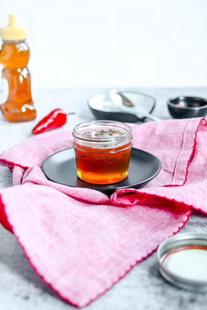 a glass jar of hot honey on a black plate on a red napkin