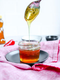 a spoon drizzling hot honey into a glass jar