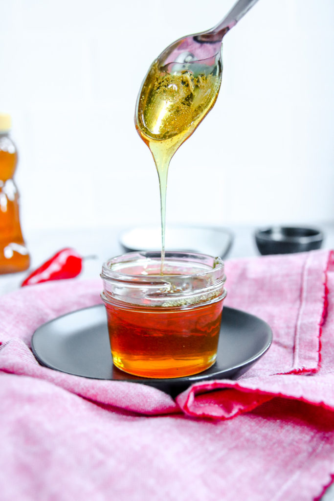 a spoon drizzling hot honey into a glass jar