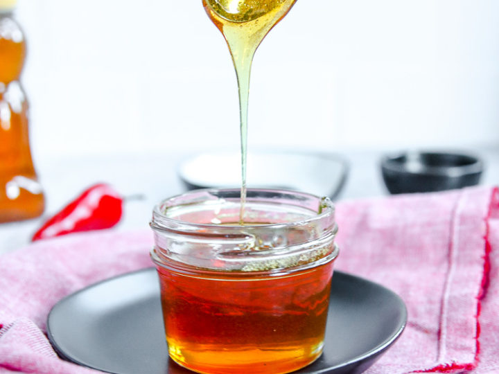 a spoon drizzling hot honey into a glass jar