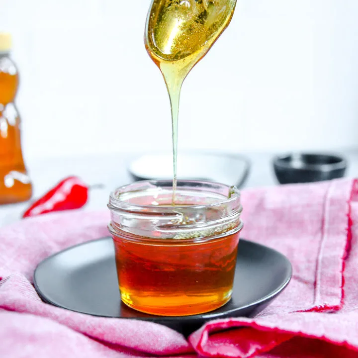 a spoon drizzling hot honey into a glass jar