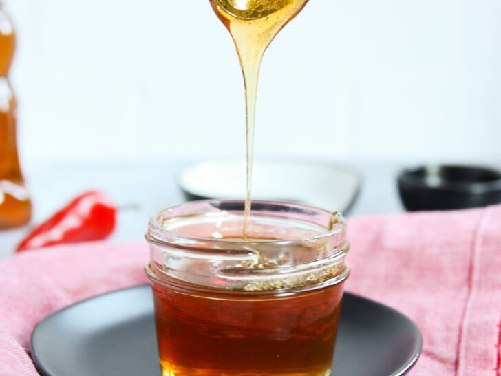 a spoon drizzling hot honey into a glass jar