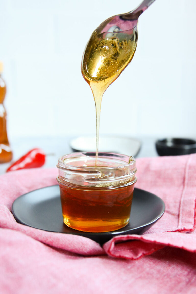 a spoon drizzling hot honey into a glass jar