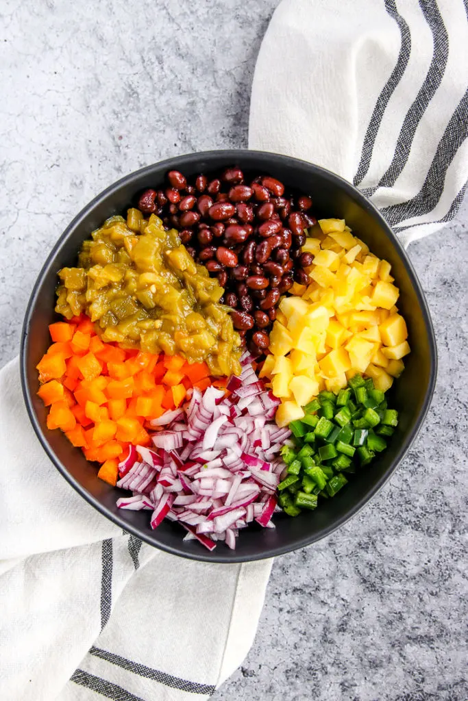 a black bowl with sections of black beans, green chiles, orange bell pepper, red onion, jalapeno, and mango