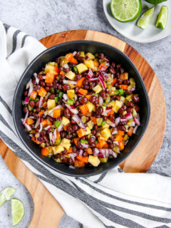 a bowl of mango black bean salsa on a wooden cutting board with limes scattered around it