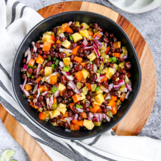 a bowl of mango black bean salsa on a wooden cutting board with limes scattered around it