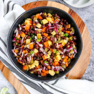 a bowl of mango black bean salsa on a wooden cutting board with limes scattered around it