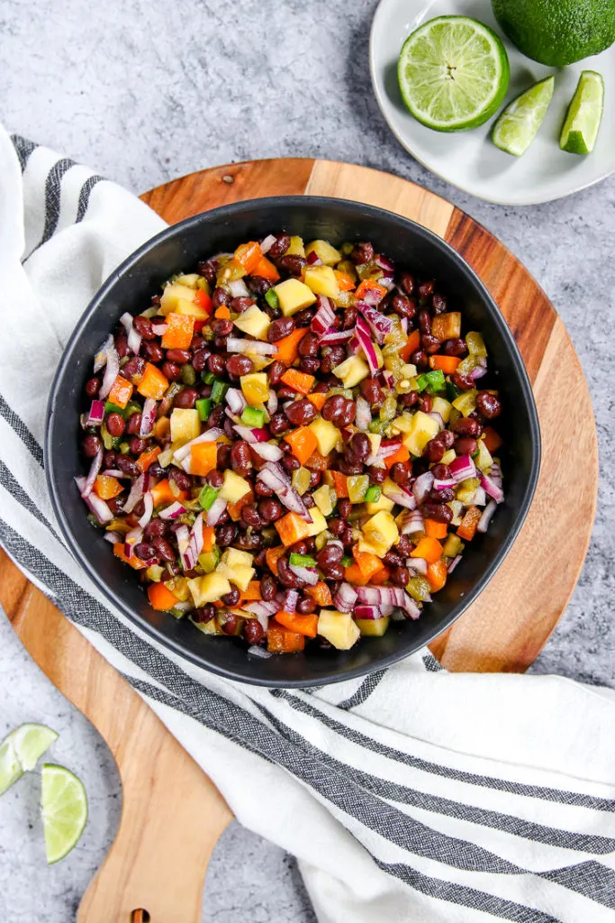 a bowl of mango black bean salsa on a wooden cutting board with limes scattered around it