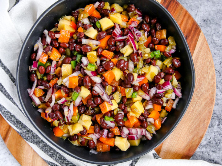 a bowl of mango black bean salsa on a wooden cutting board with limes scattered around it