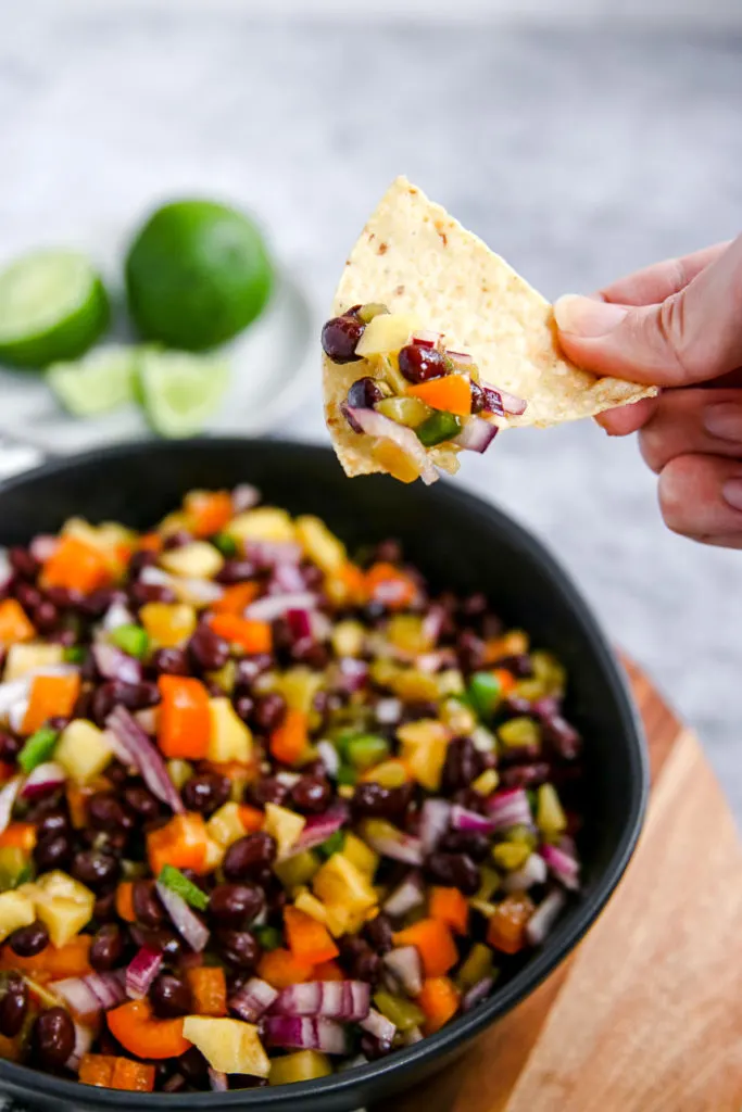 a hand holding a tortilla chip with mango black bean salsa on it