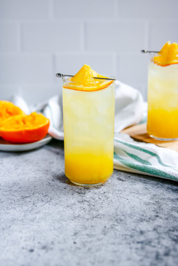 a highball glass filled with an orange crush and an orange slice on top