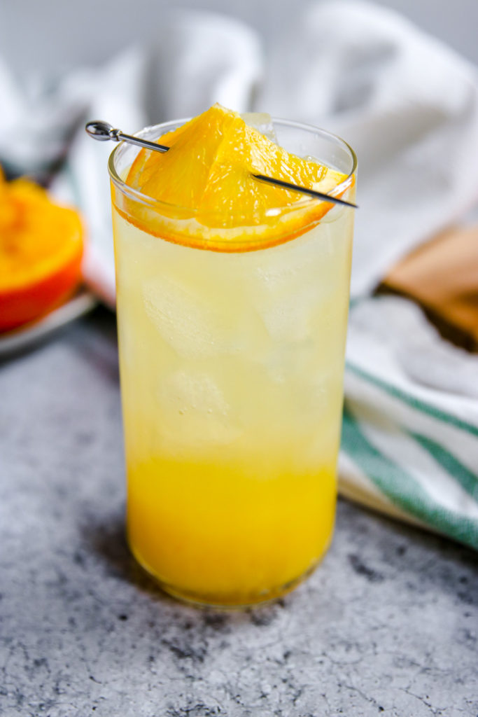 a closeup of a sliced orange in a cocktail pick on top of the glass