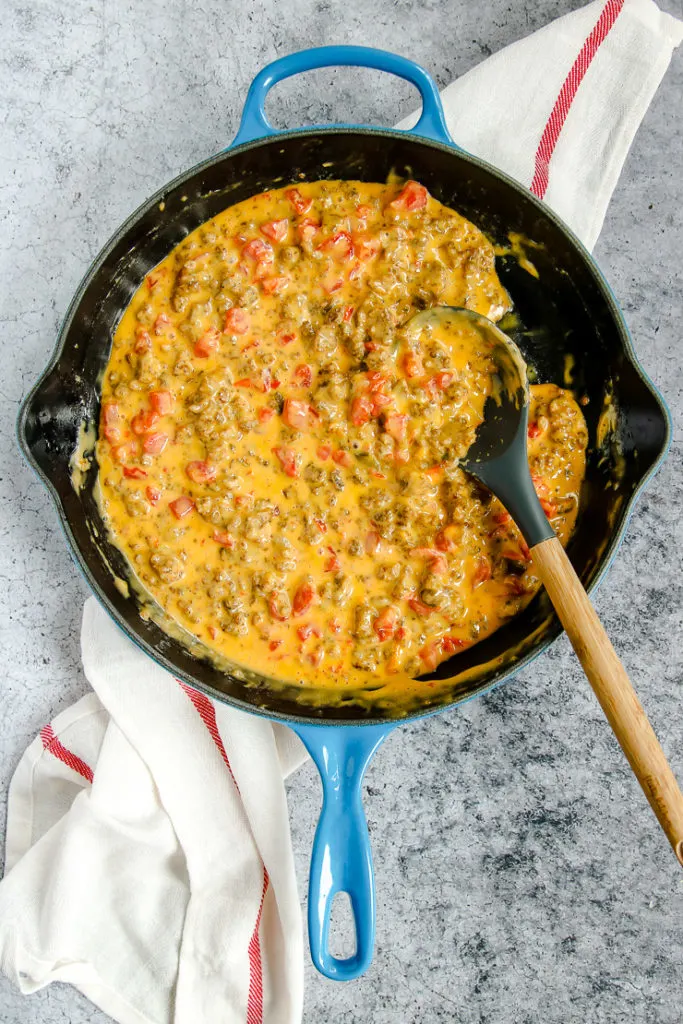 a blue enameled cast iron pan with rotel sausage dip and a spoon