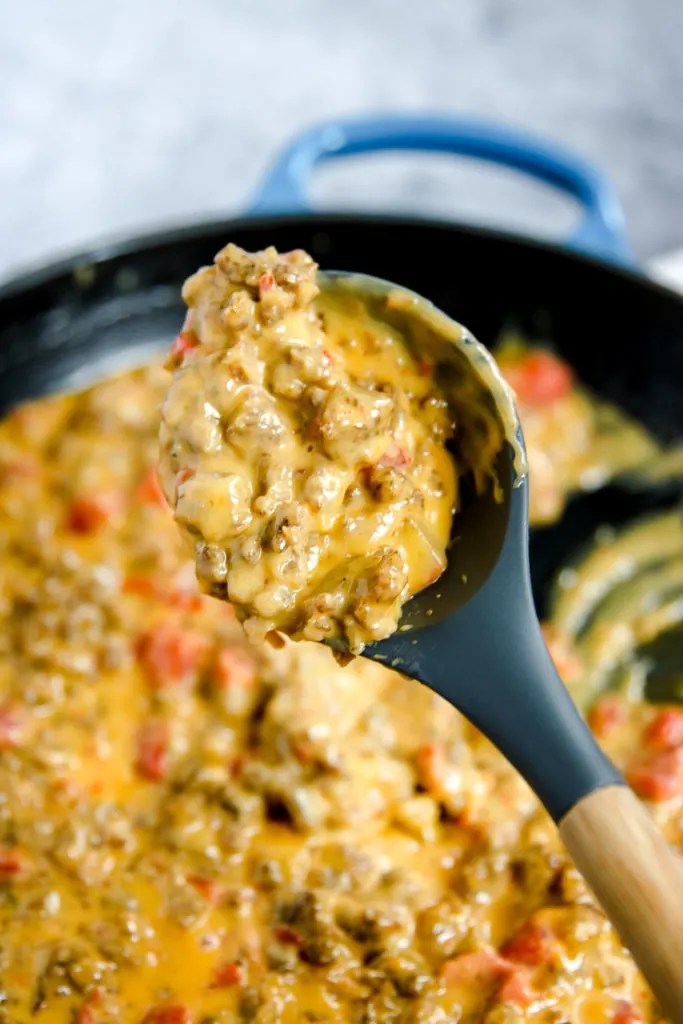 a spoon holding up rotel sausage dip over the cast iron pan