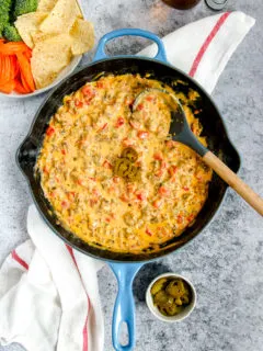 a blue cast iron enameled pan with rotel sausage dip next to chips and a beer