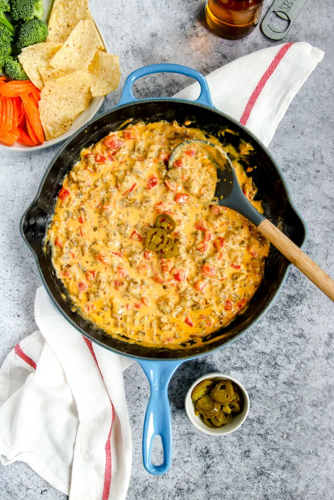 a blue cast iron enameled pan with rotel sausage dip next to chips and a beer