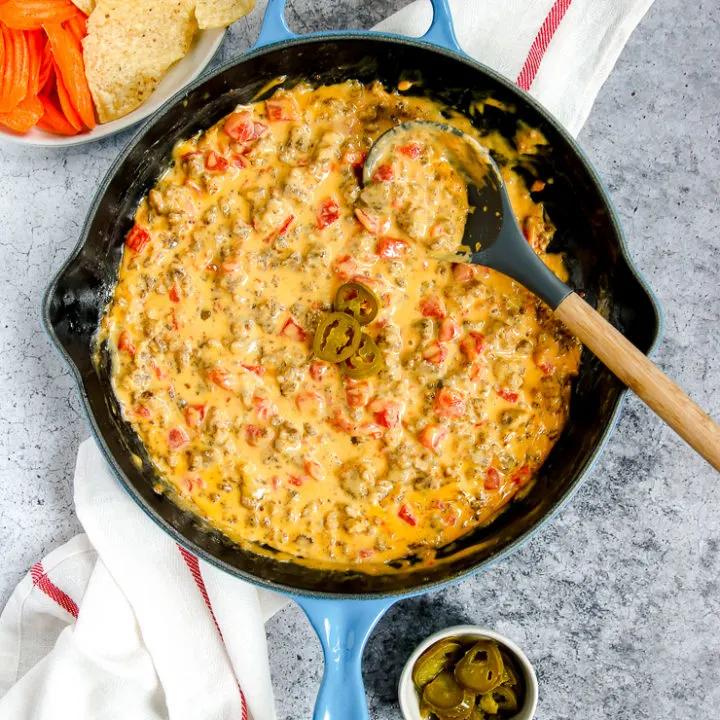 a blue cast iron enameled pan with rotel sausage dip next to chips and a beer