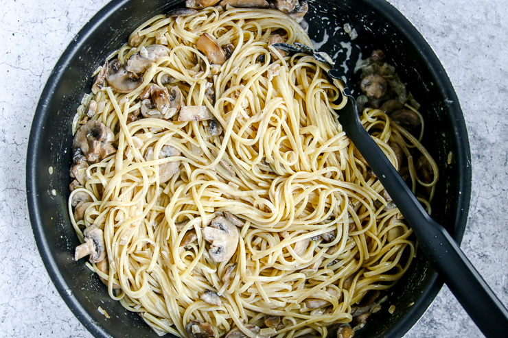 a skillet of white wine mushroom pasta being stirred together