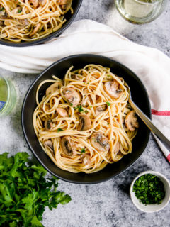 white wine mushroom pasta in a black bowl next to a glass of white wine and parsley