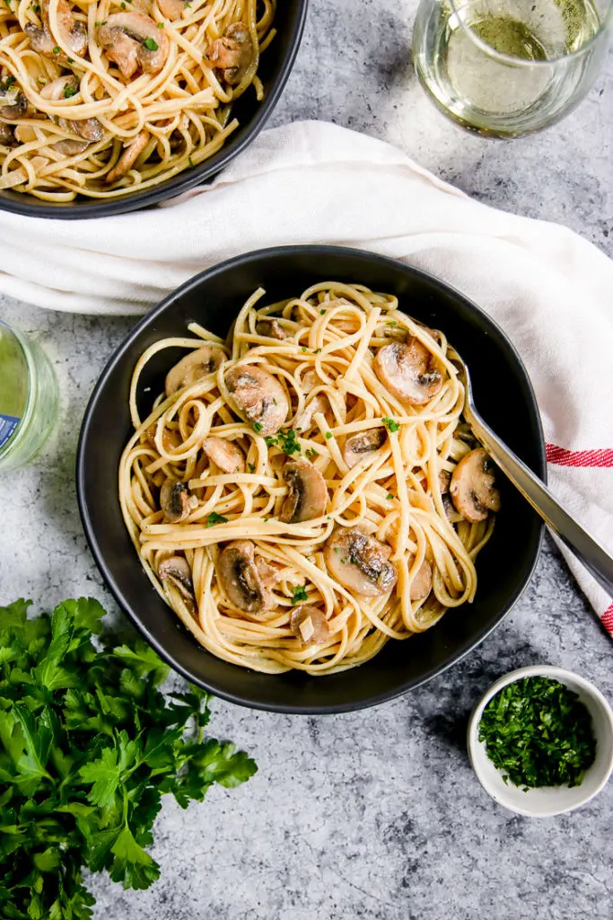 white wine mushroom pasta in a black bowl next to a glass of white wine and parsley