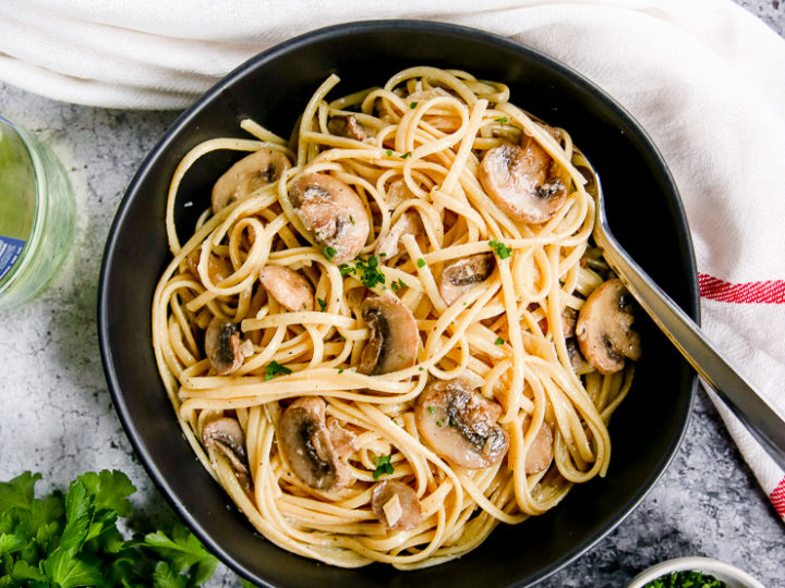 white wine mushroom pasta in a black bowl next to a glass of white wine and parsley