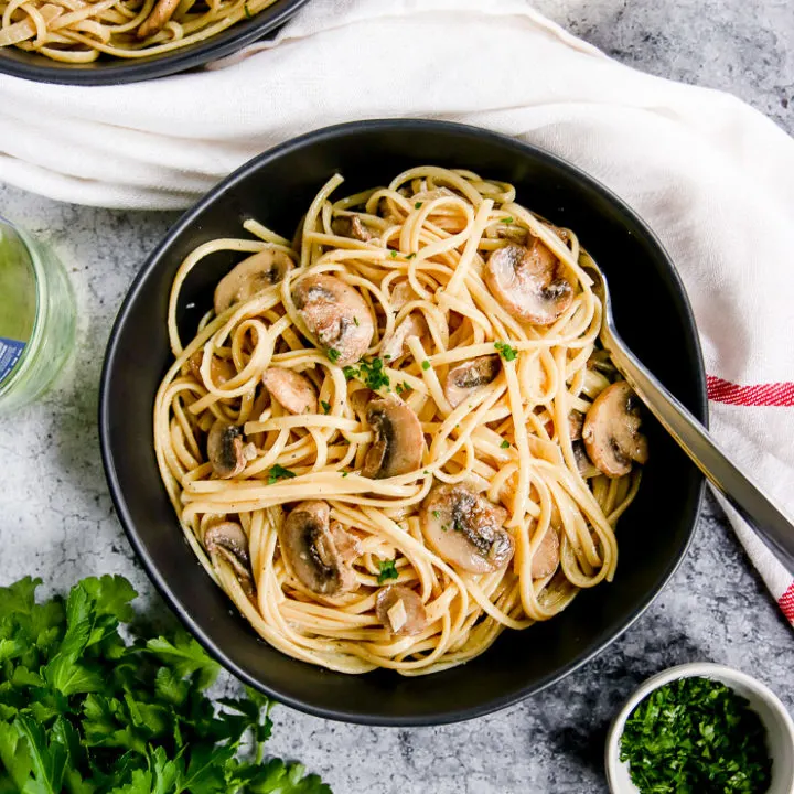 white wine mushroom pasta in a black bowl next to a glass of white wine and parsley