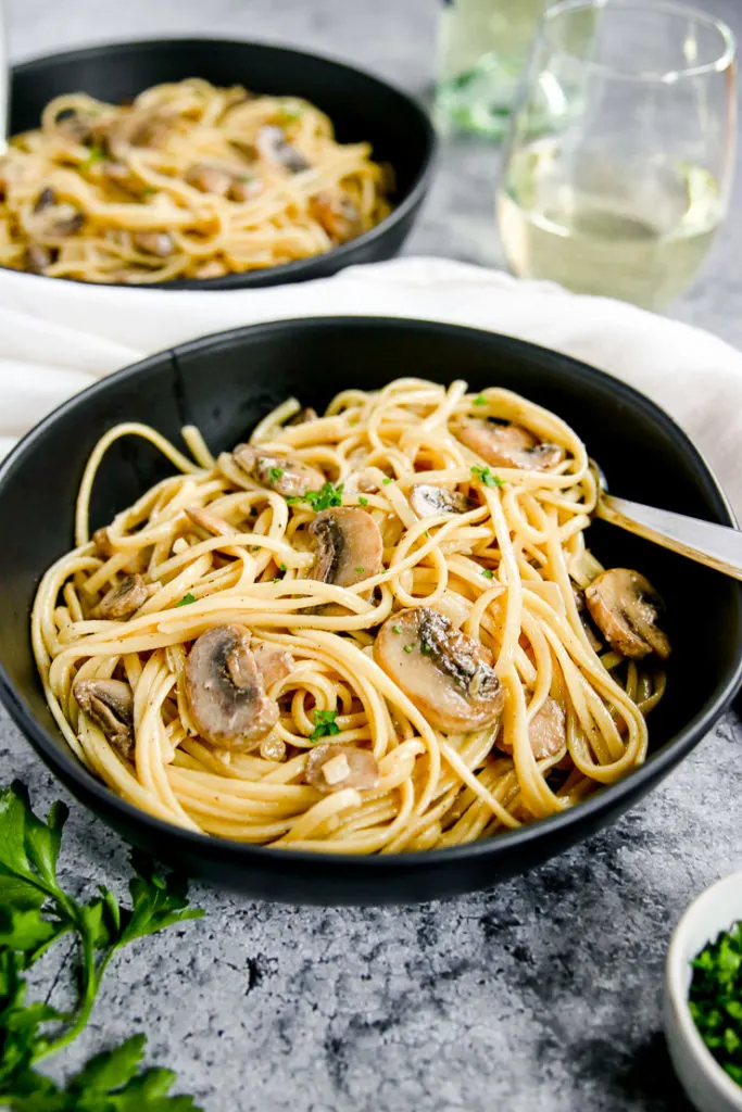 a close up of white wine mushroom pasta in a bowl with a fork in it