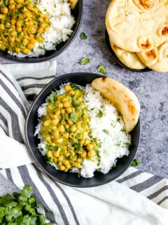two black bowls full of rice, naan, and chickpea coconut curry
