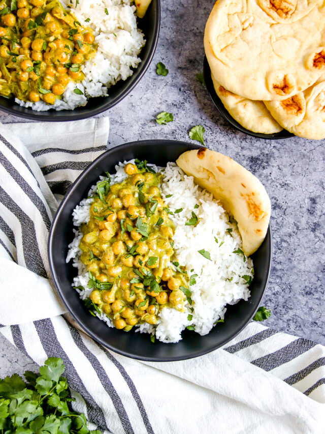 two black bowls full of rice, naan, and chickpea coconut curry