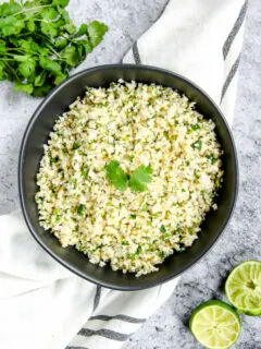 a black bowl on a striped napkin with cilantro lime cauliflower rice in it