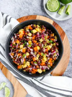 a bowl of mango black bean salsa on a wooden cutting board with limes scattered around it