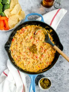 a blue cast iron enameled pan with rotel sausage dip next to chips and a beer