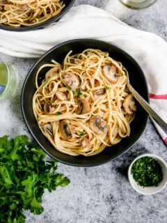 white wine mushroom pasta in a black bowl next to a glass of white wine and parsley