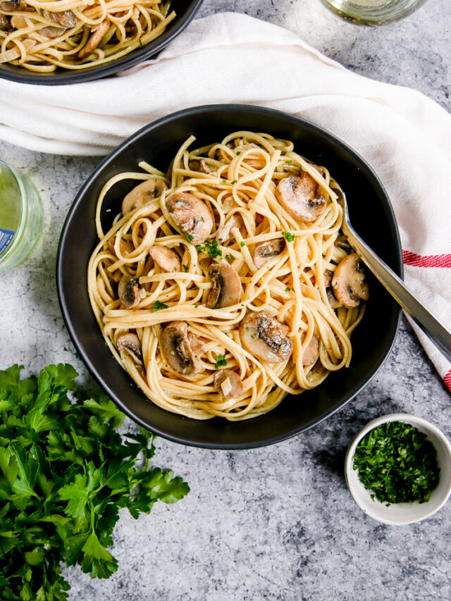 white wine mushroom pasta in a black bowl next to a glass of white wine and parsley