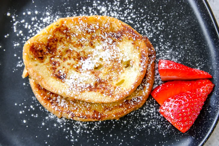 a close up of a piece of french toast with powdered sugar and cut strawberries