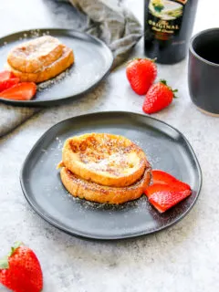 two plates of baileys french toast with strawberries, a mug of coffee, and bottle of baileys