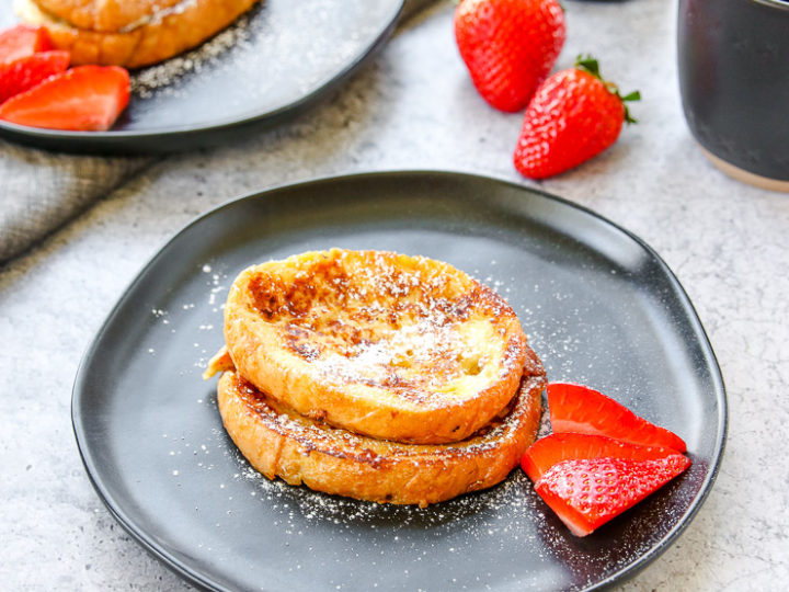 two plates of baileys french toast with strawberries, a mug of coffee, and bottle of baileys