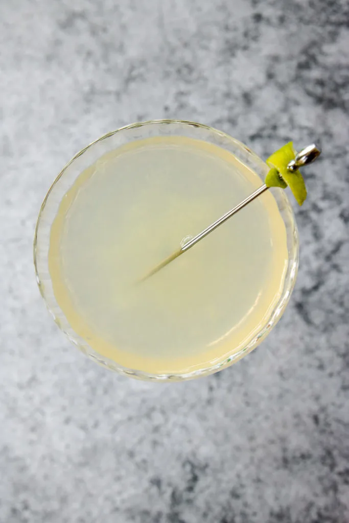 overhead shot of the coupe glass full of pastel elderflower gimlet and a cocktail pick