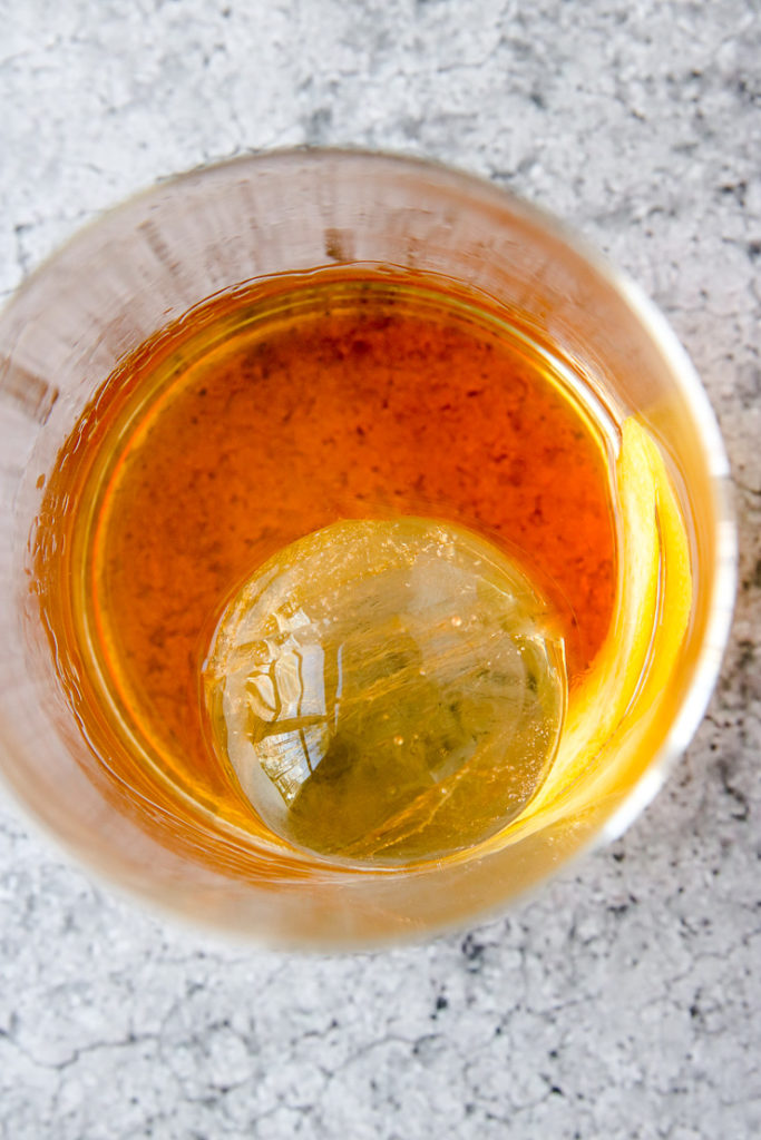 an overhead shot of a large round ice cube in a rocks glass with liquor