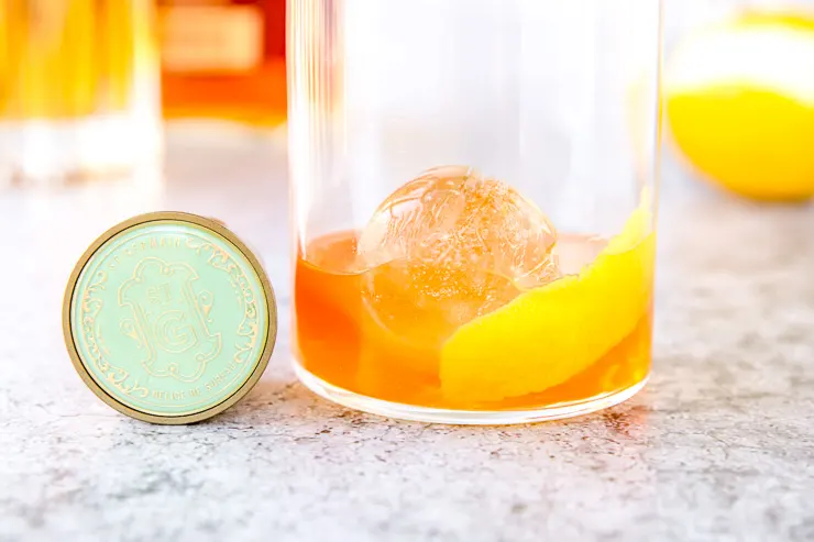 a close up of an elderflower old fashioned and the teal lid of st. germain