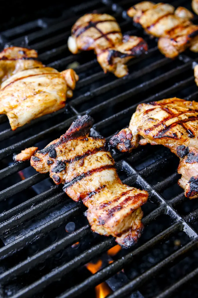 boneless skinless chicken thighs with grill marks on the grill over a flame