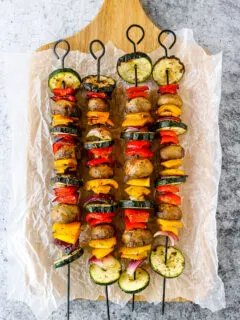 four grilled veggie skewers on wax paper on a wooden platter