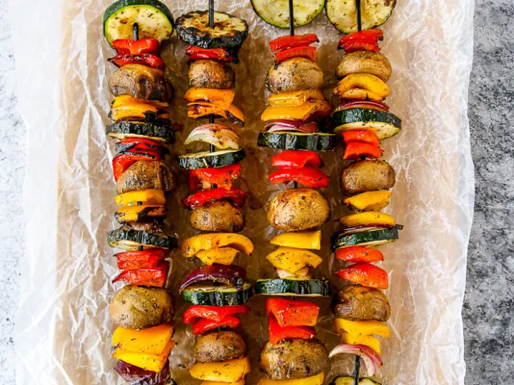 four grilled veggie skewers on wax paper on a wooden platter