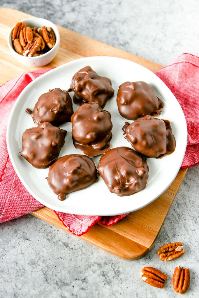 a plate of chocolate covered pecan turtles on a wooden board and a red napkin