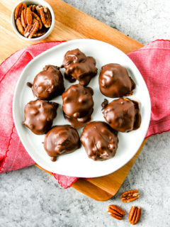 an overhead shot of a white plate with chocolate covered pecan turtles with pecans around the plate