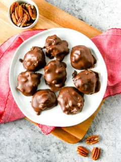 an overhead shot of a white plate with chocolate covered pecan turtles with pecans around the plate