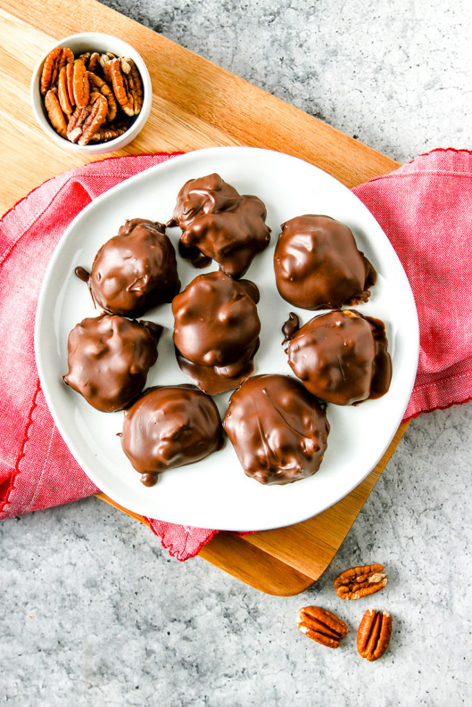 an overhead shot of a white plate with chocolate covered pecan turtles with pecans around the plate