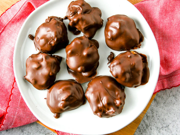 an overhead shot of a white plate with chocolate covered pecan turtles with pecans around the plate